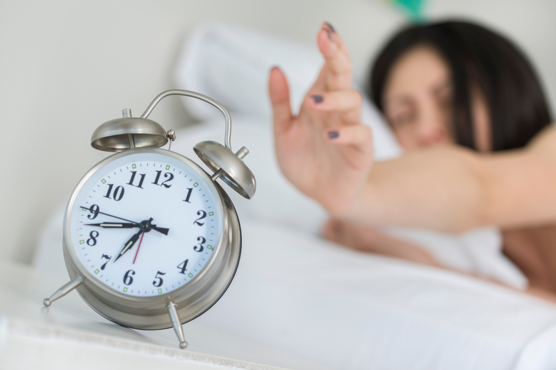 picture of a woman in bed reaching out to snooze her alarm clock