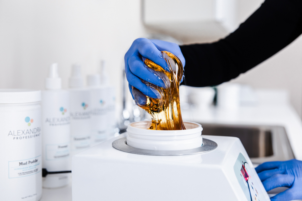 Picture of a certified Alexandria Professional sugaring practitioner removing some amber colored all-natural sugar paste from a jar of sugar before a treatment.